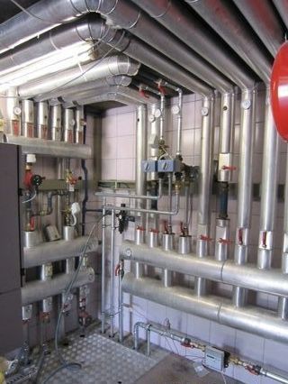 Industrieller Maschinenraum mit silbernen Rohren, Ventilen und Messgeräten, die einen metallischen Versorgungsraum durchziehen.