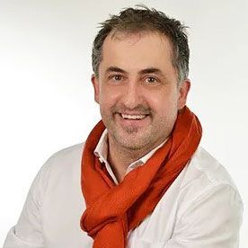 Lächelnder Mann in weißem Hemd mit leuchtend orangefarbenem Schal vor schlichtem weißen Hintergrund