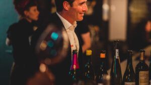 Un hombre con traje está parado frente a una fila de botellas de vino.