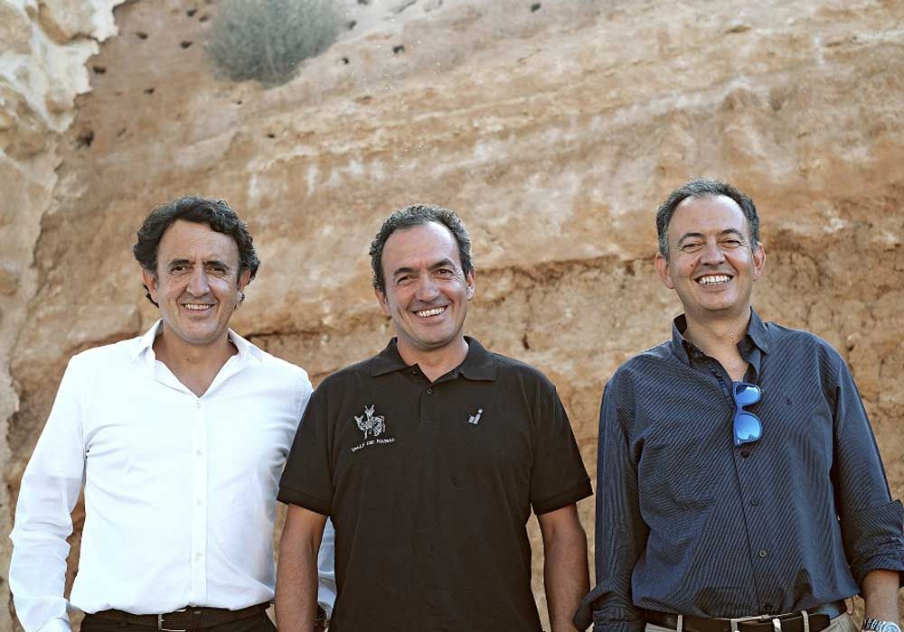 Tres hombres posan para una foto frente a una pared de roca.