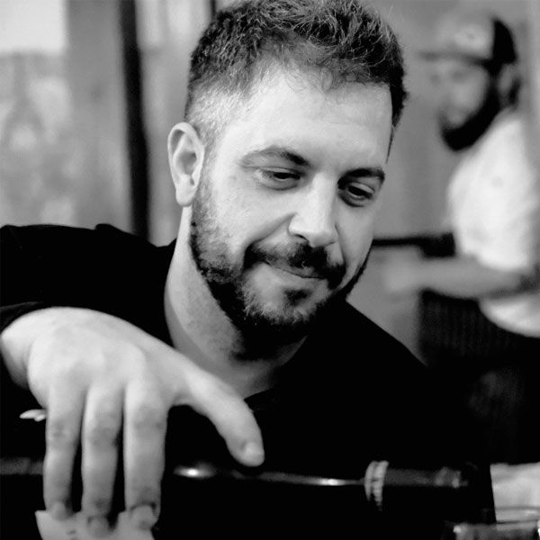 Un hombre con barba está sentado en una mesa sosteniendo una botella de vino.