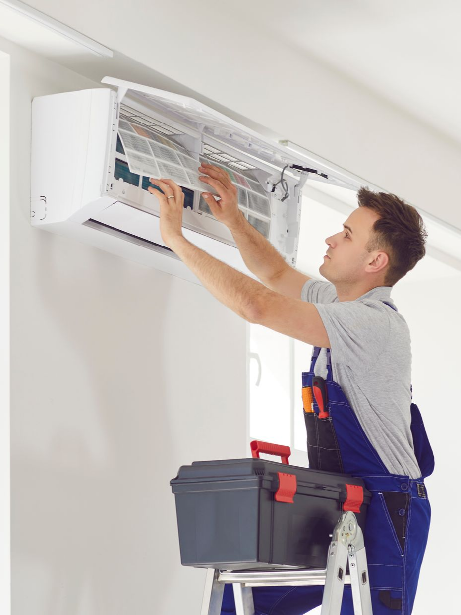 Un homme en salopette bleue répare un climatiseur mural.