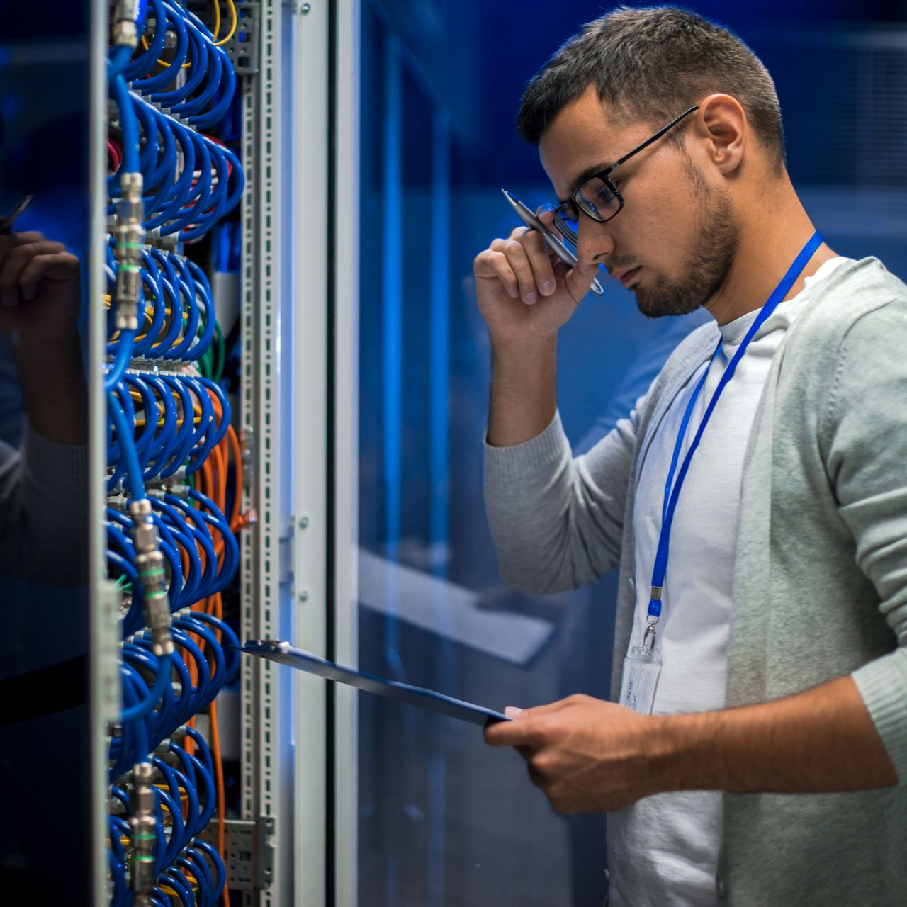 Un homme portant des lunettes et tenant un bloc-notes examine des serveurs informatiques.