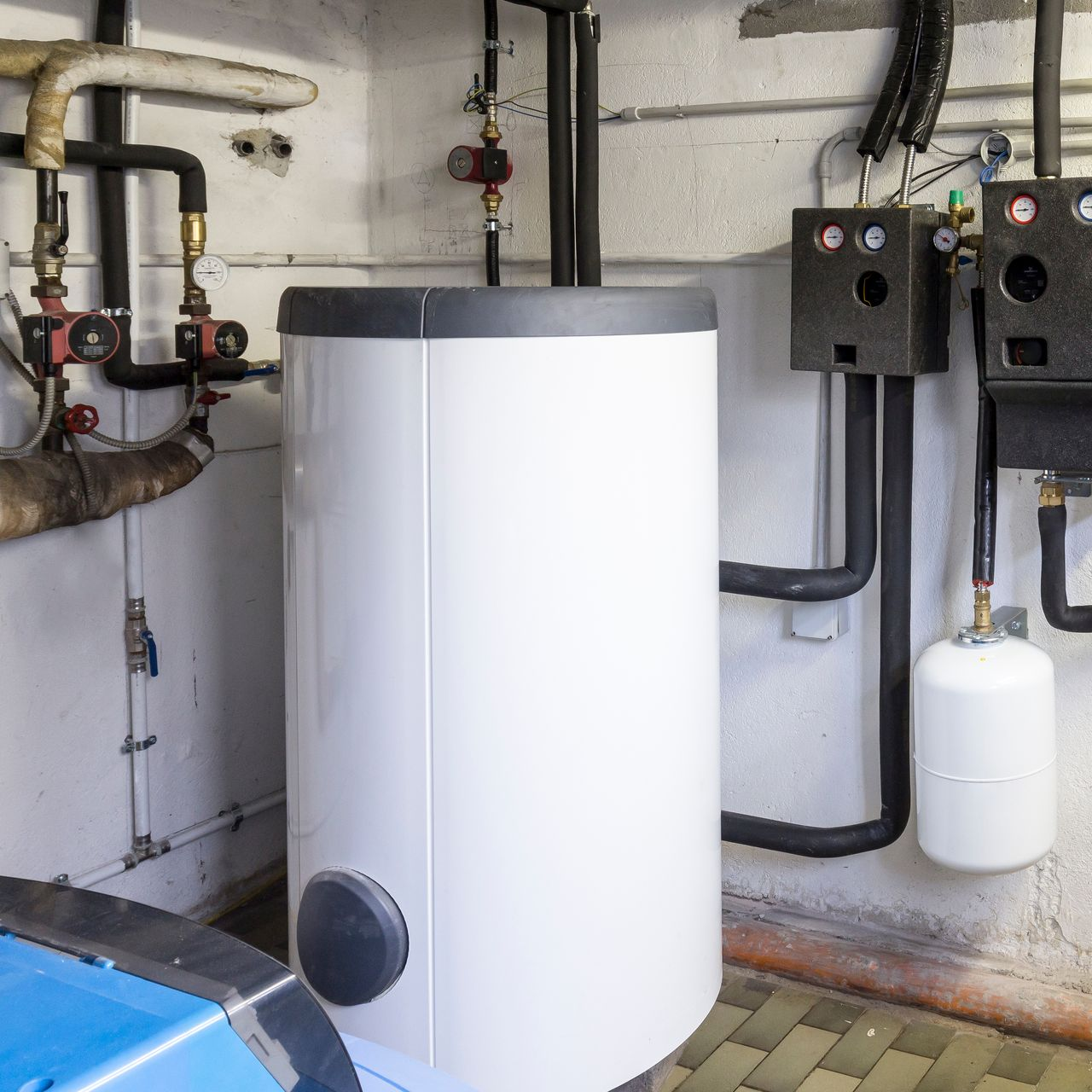 Chauffe-eau thermodynamique blanc dans une buanderie, avec des tuyaux et panneaux de commande.