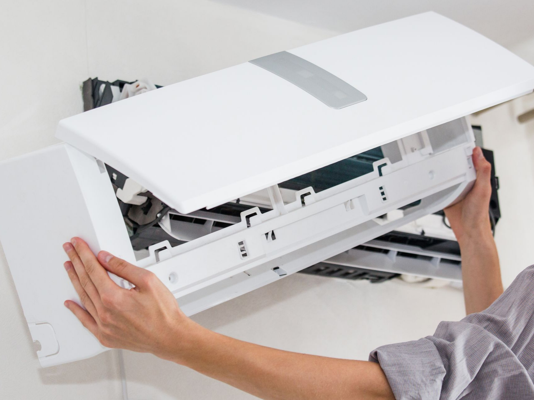 Une personne retire le couvercle d'un climatiseur mural.