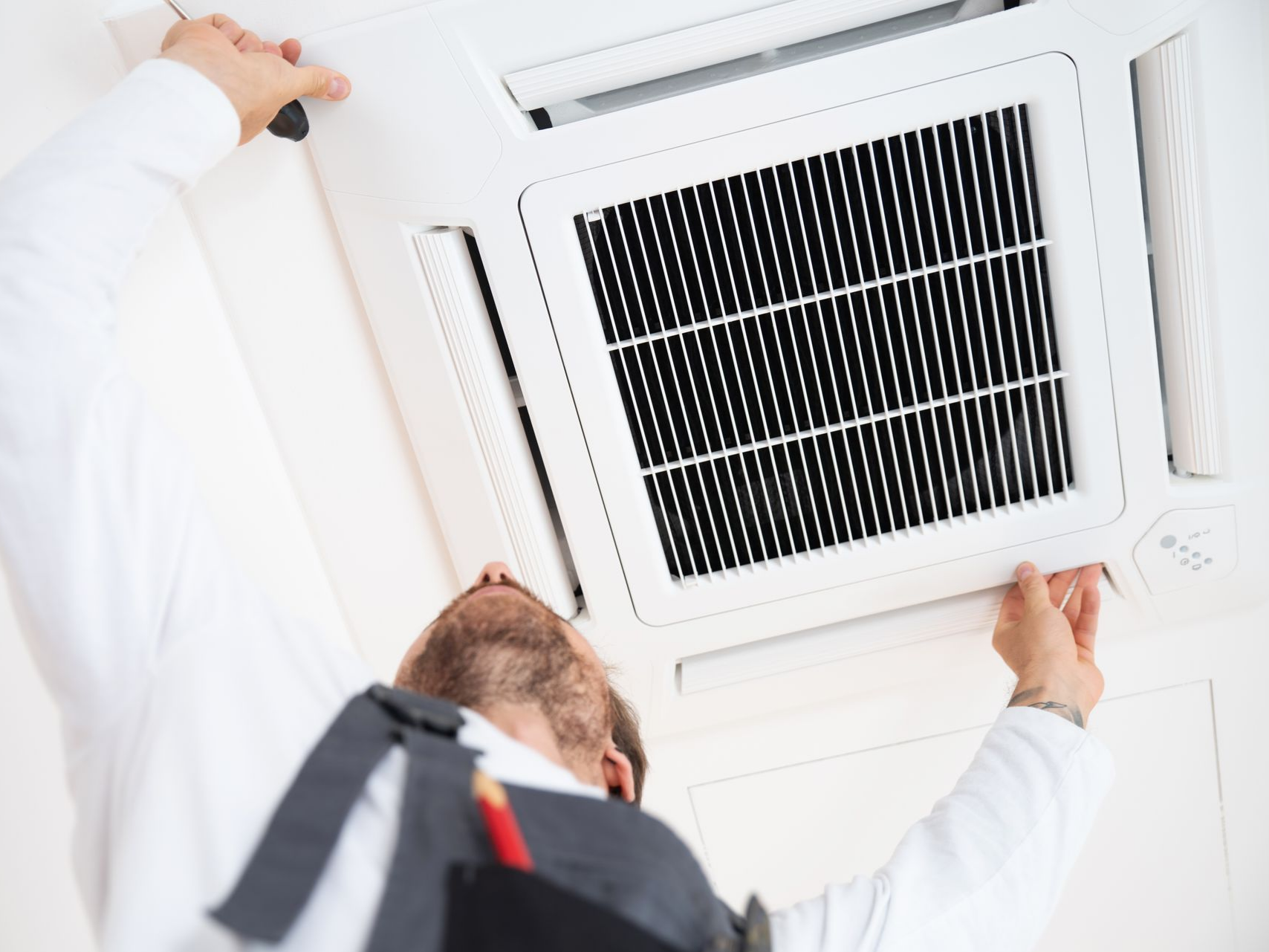 Une personne installe un climatiseur fixé au plafond.
