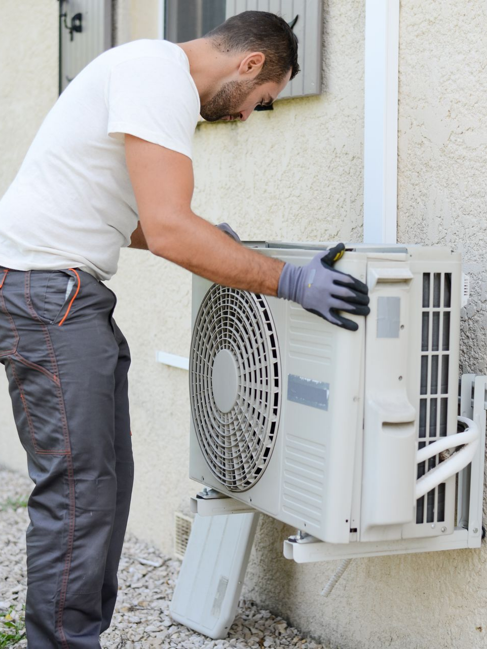 Un homme portant des gants installe un climatiseur extérieur sur un bâtiment.