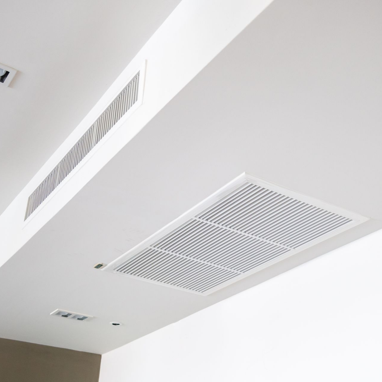 Plafond blanc avec grilles d'aération rectangulaires.