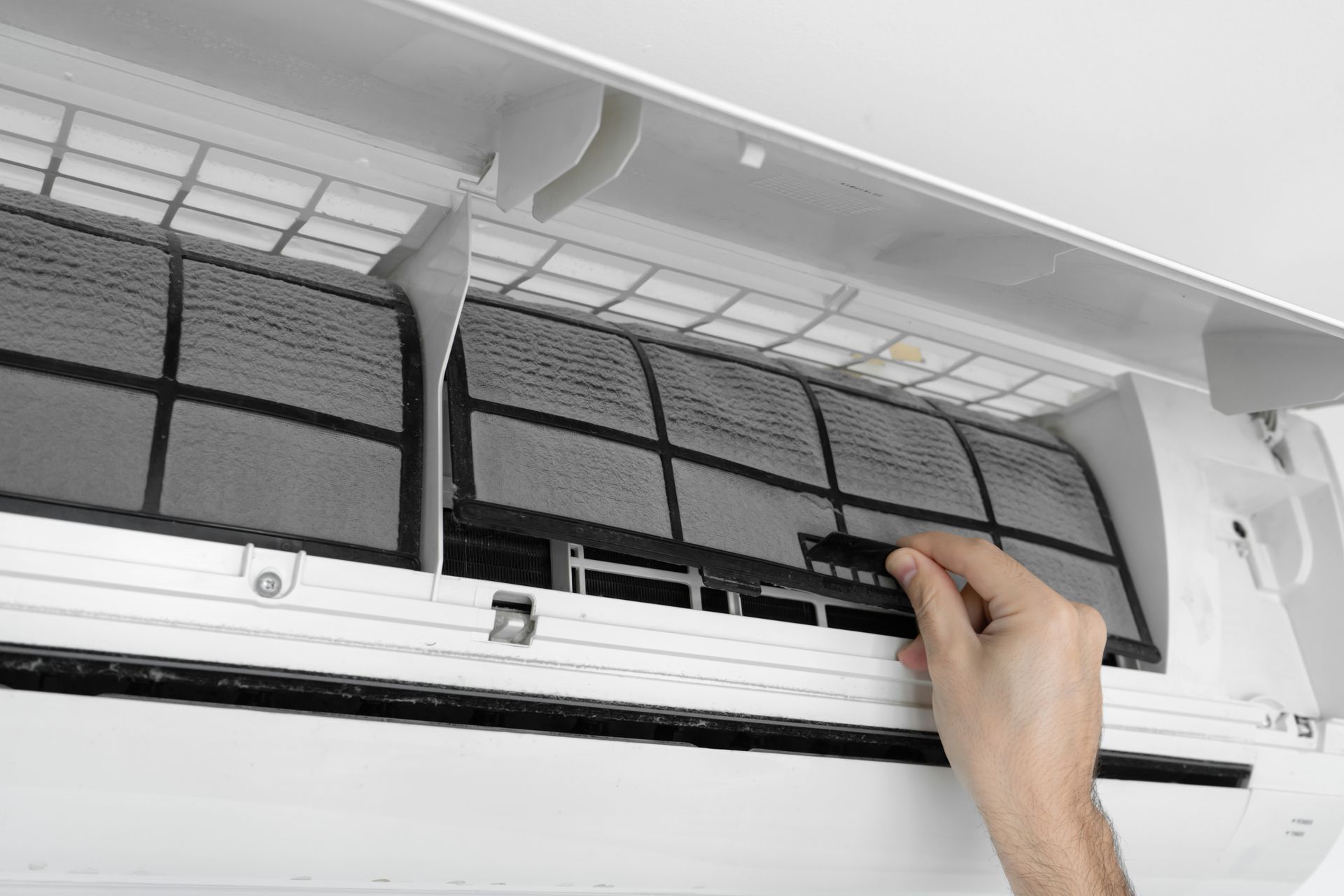 Une personne retire le filtre à air encrassé d'un climatiseur mural.