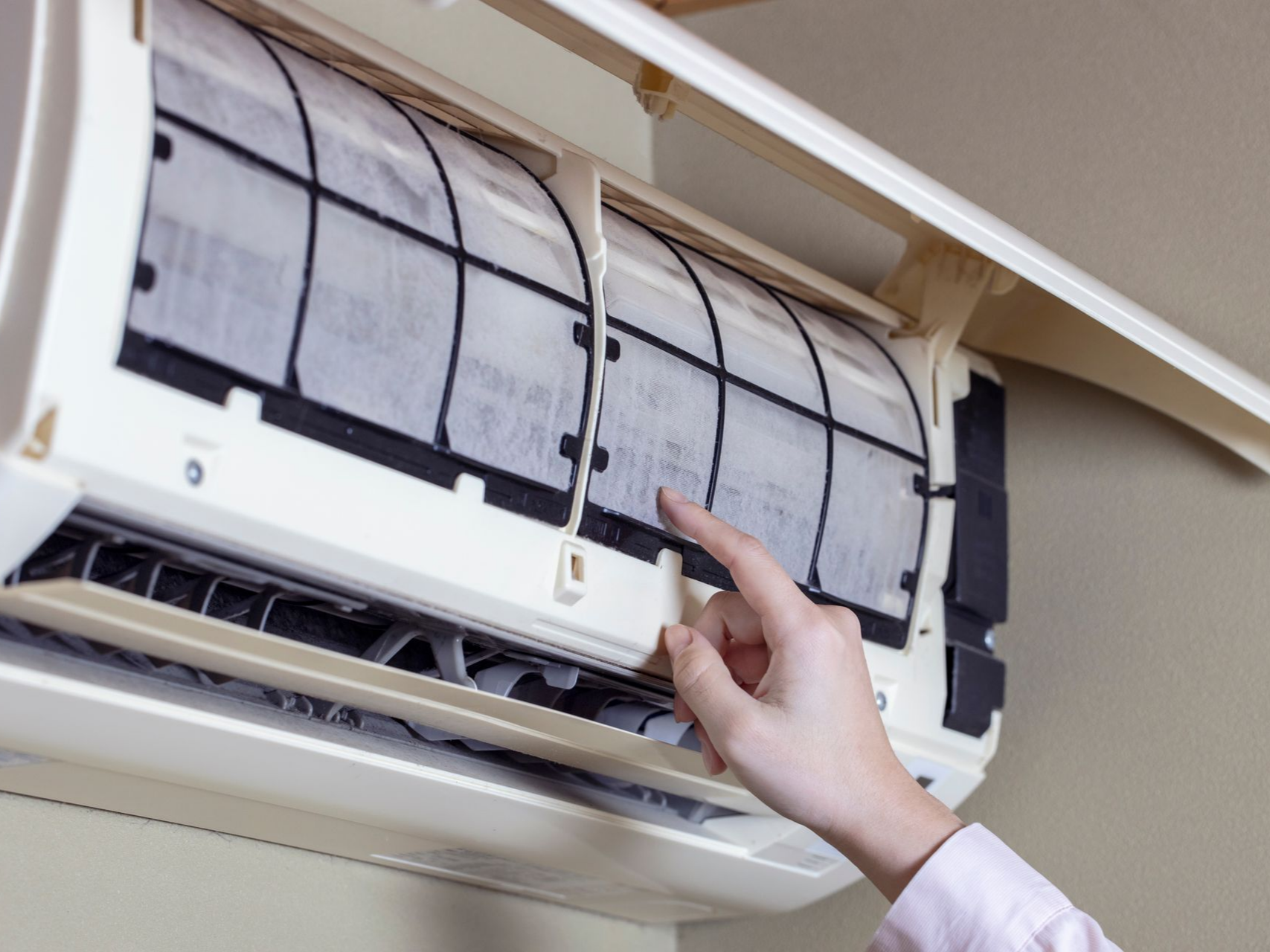 La main d'une personne touche un filtre de climatisation à l'intérieur d'un climatiseur fixé au mur.