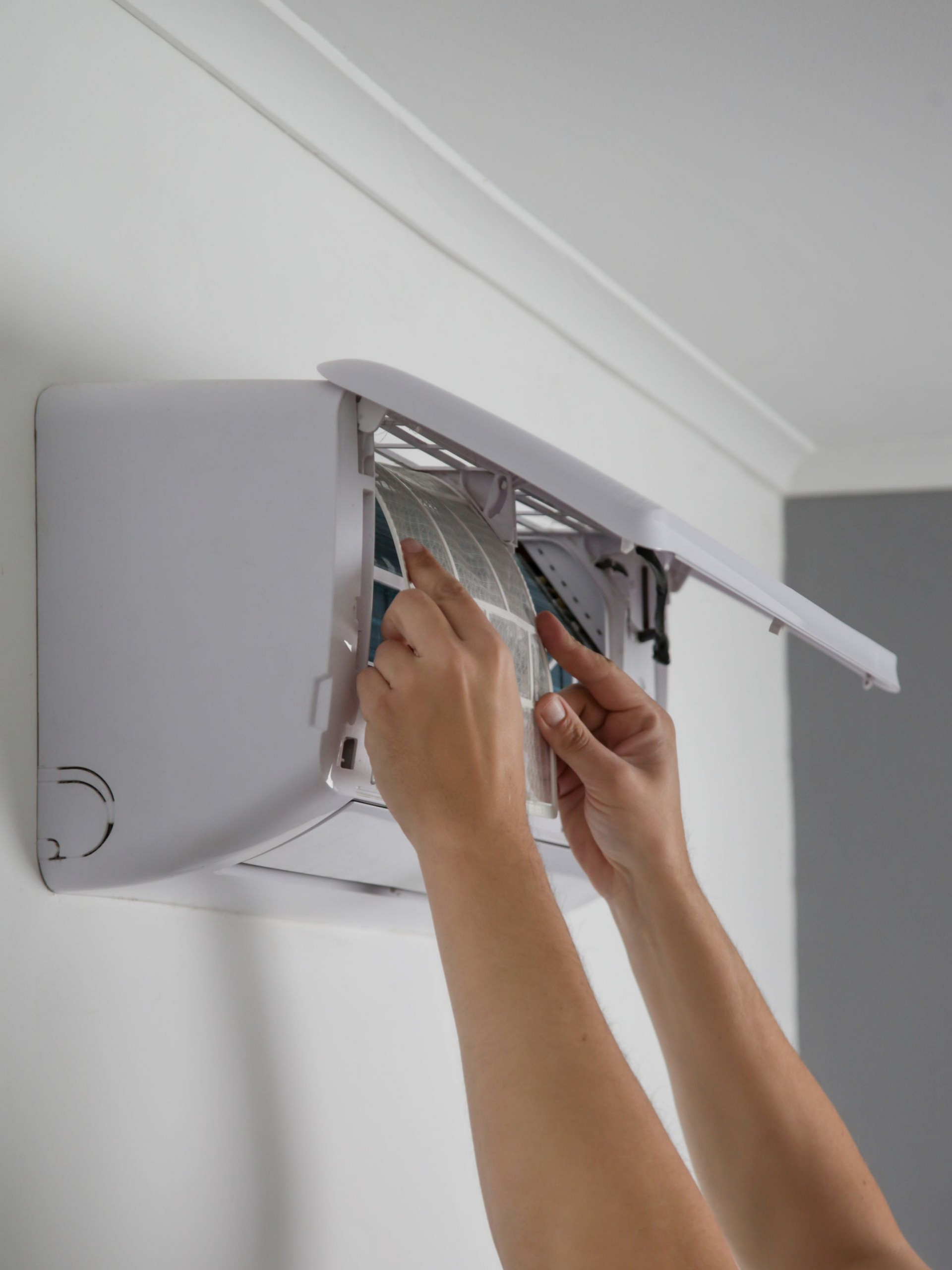 Une personne nettoie le filtre d'un climatiseur fixé au mur.