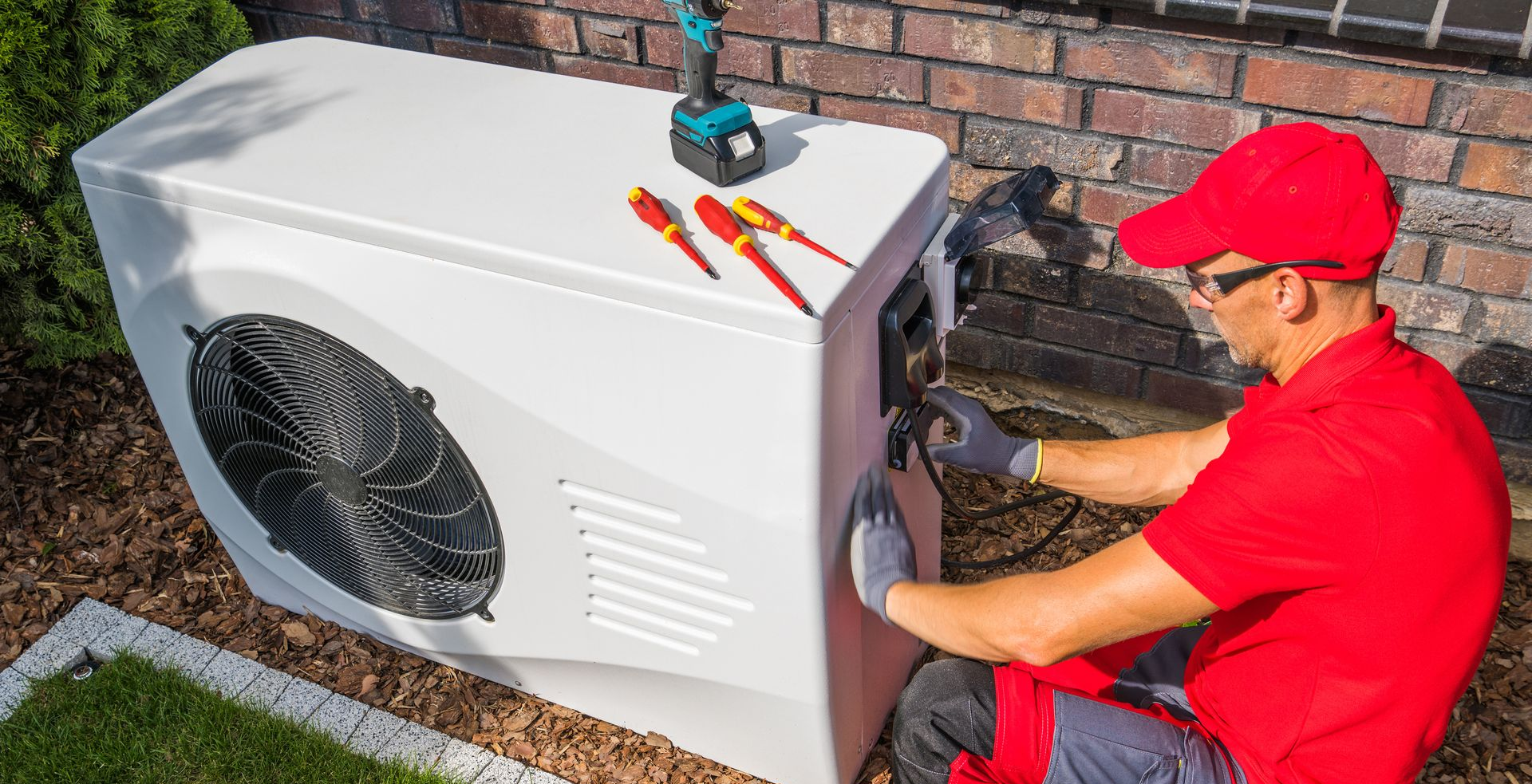 Un technicien en climatisation travaille sur une unité blanche extérieure.