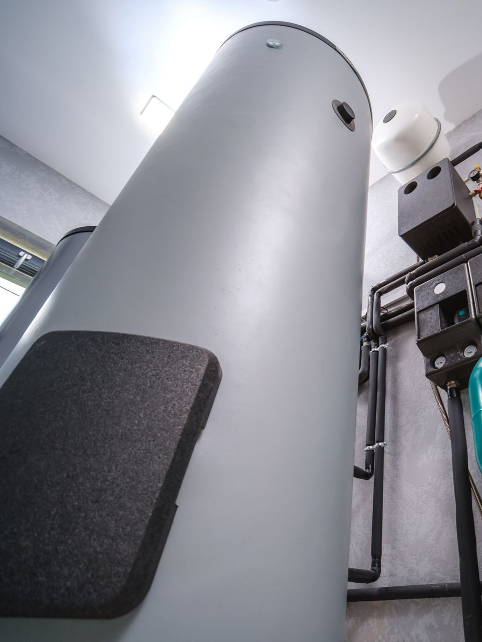 Grand chauffe-eau thermodynamique avec des tuyaux et autres composants de plomberie dans une buanderie.