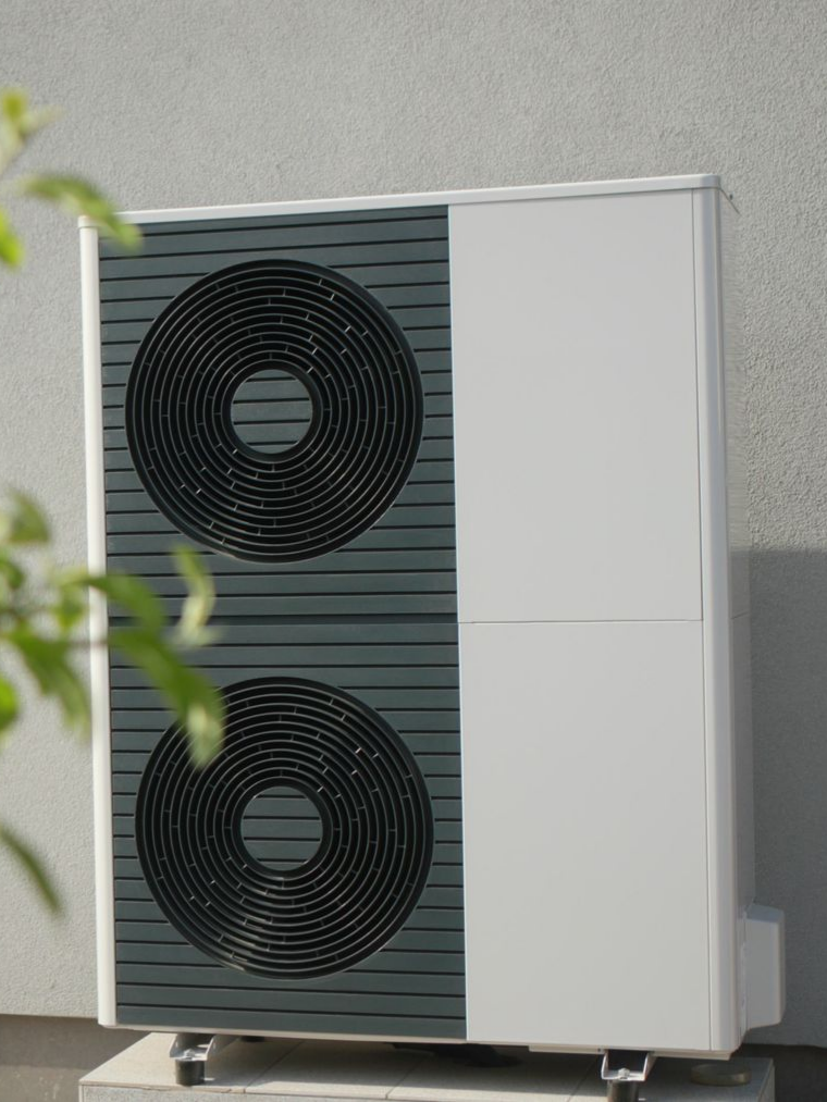 Unité de pompe à chaleur contre un mur gris clair.
