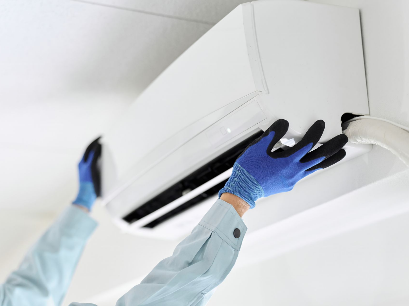Une personne portant des gants bleus installe un climatiseur mural blanc.