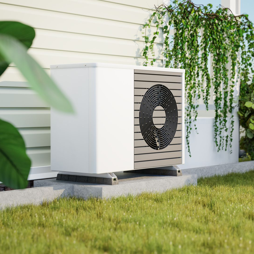 Unité extérieure de pompe à chaleur blanche sur une dalle de béton, entourée de végétation.