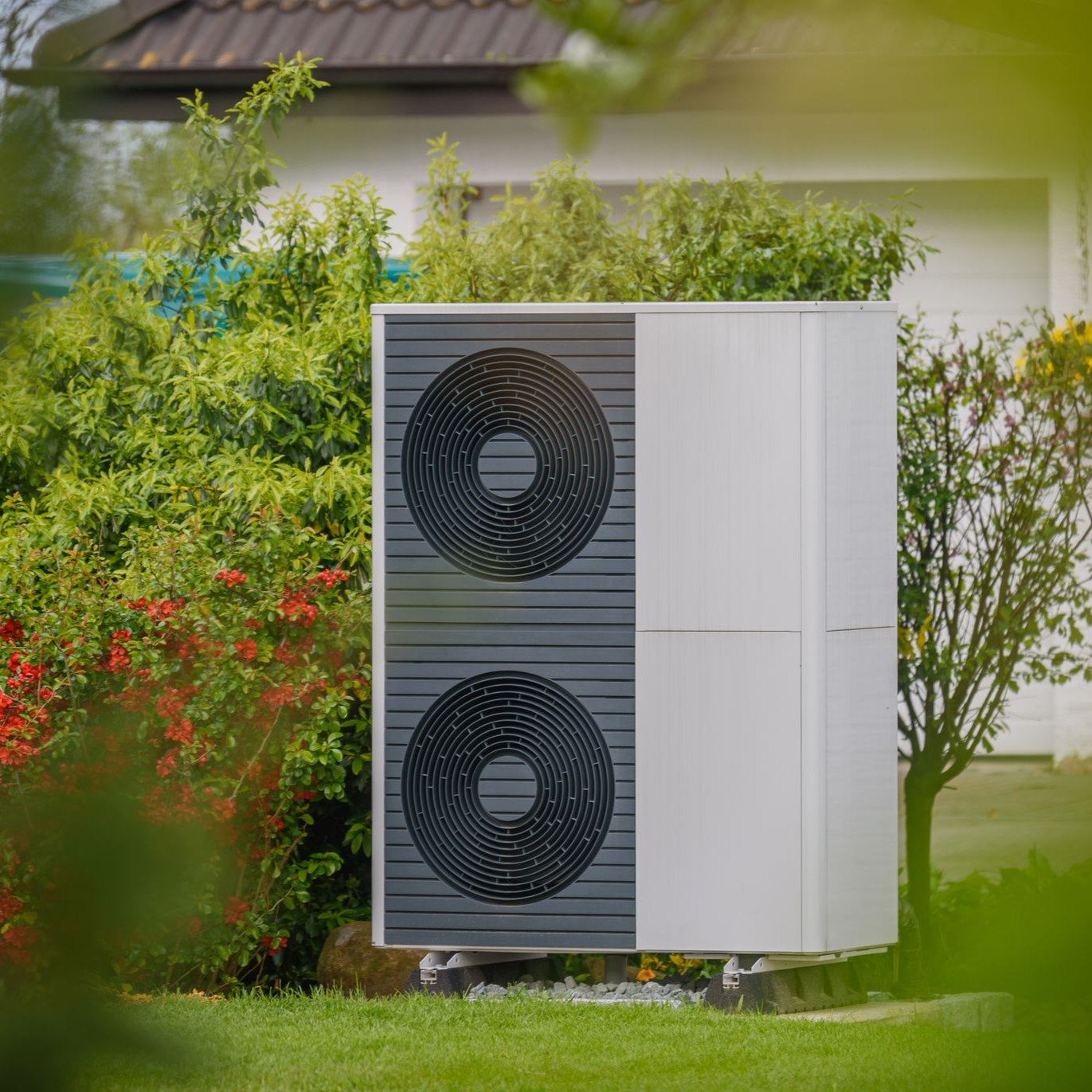 Unité extérieure de pompe à chaleur dans une cour, entourée d'arbustes verts.
