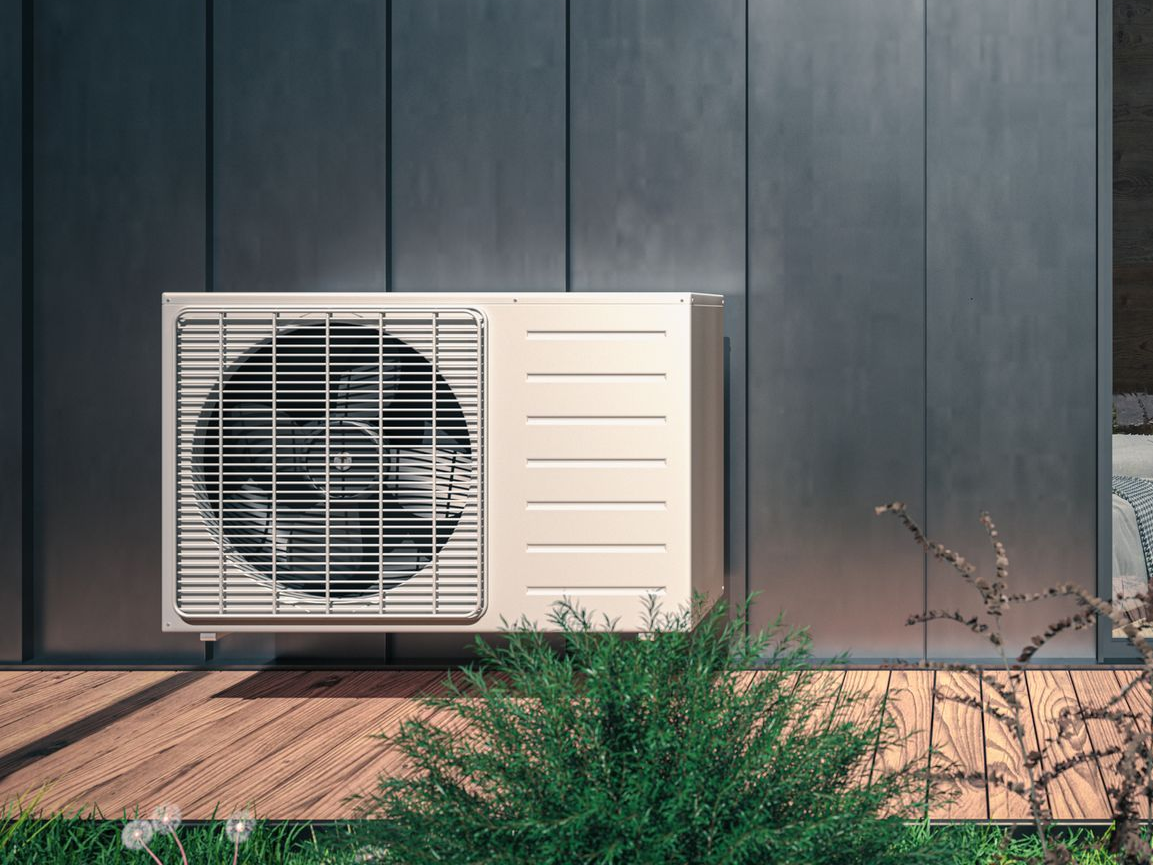 Unité de pompe à chaleur extérieure fixée sur un mur gris foncé.