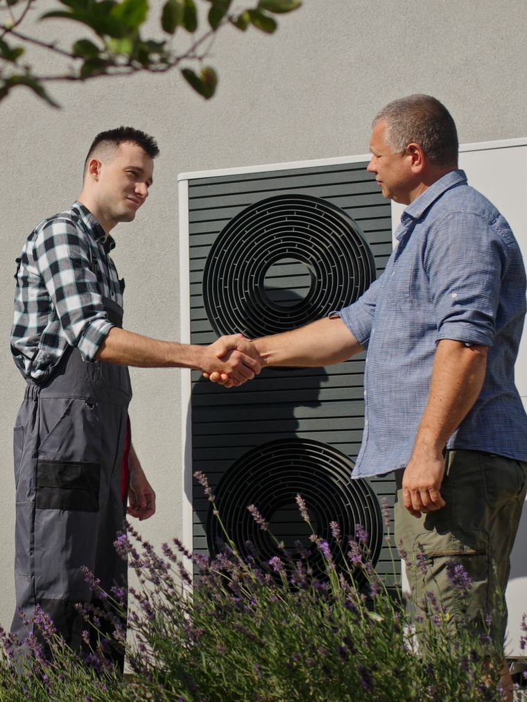 Un technicien et un particulier se serrent la main devant une unité extérieure de pompe à chaleur.