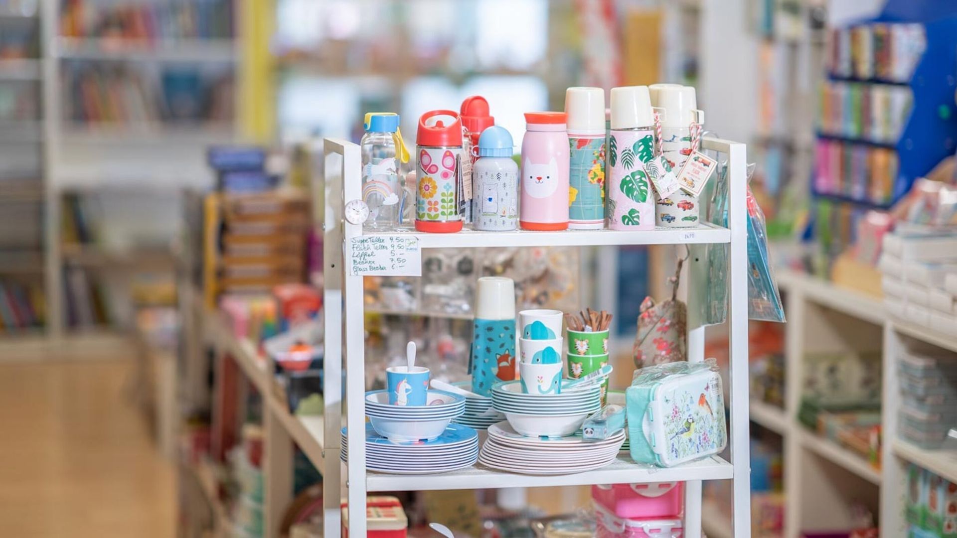 Regal mit bunten Flaschen, Tellern und Schüsseln in einem Geschäft, möglicherweise einem Kinderladen.