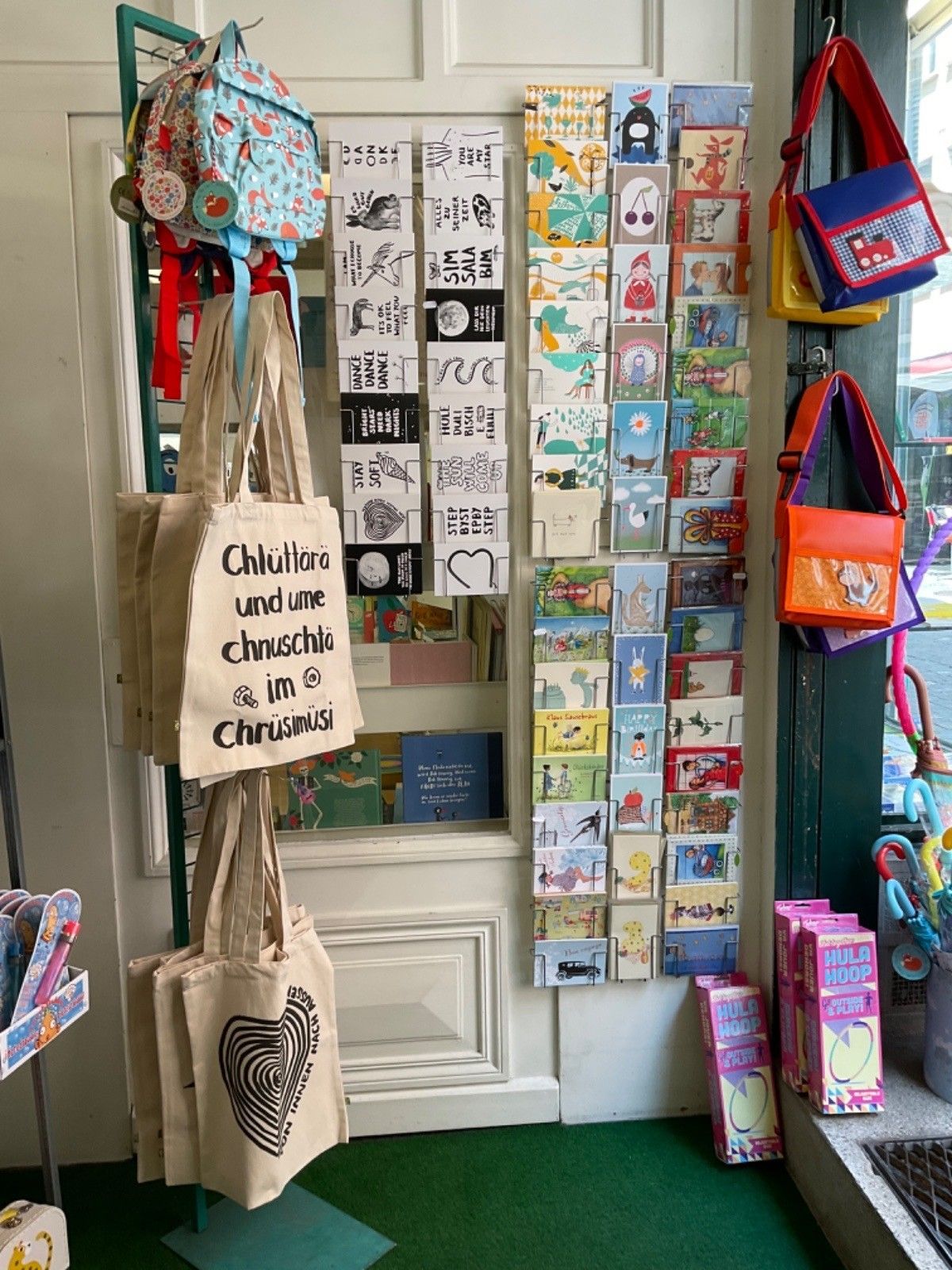 Ausstellung von Karten, Taschen und Rucksäcken in einem Geschäft mit verschiedenen Designs und einer Holztür im Hintergrund.