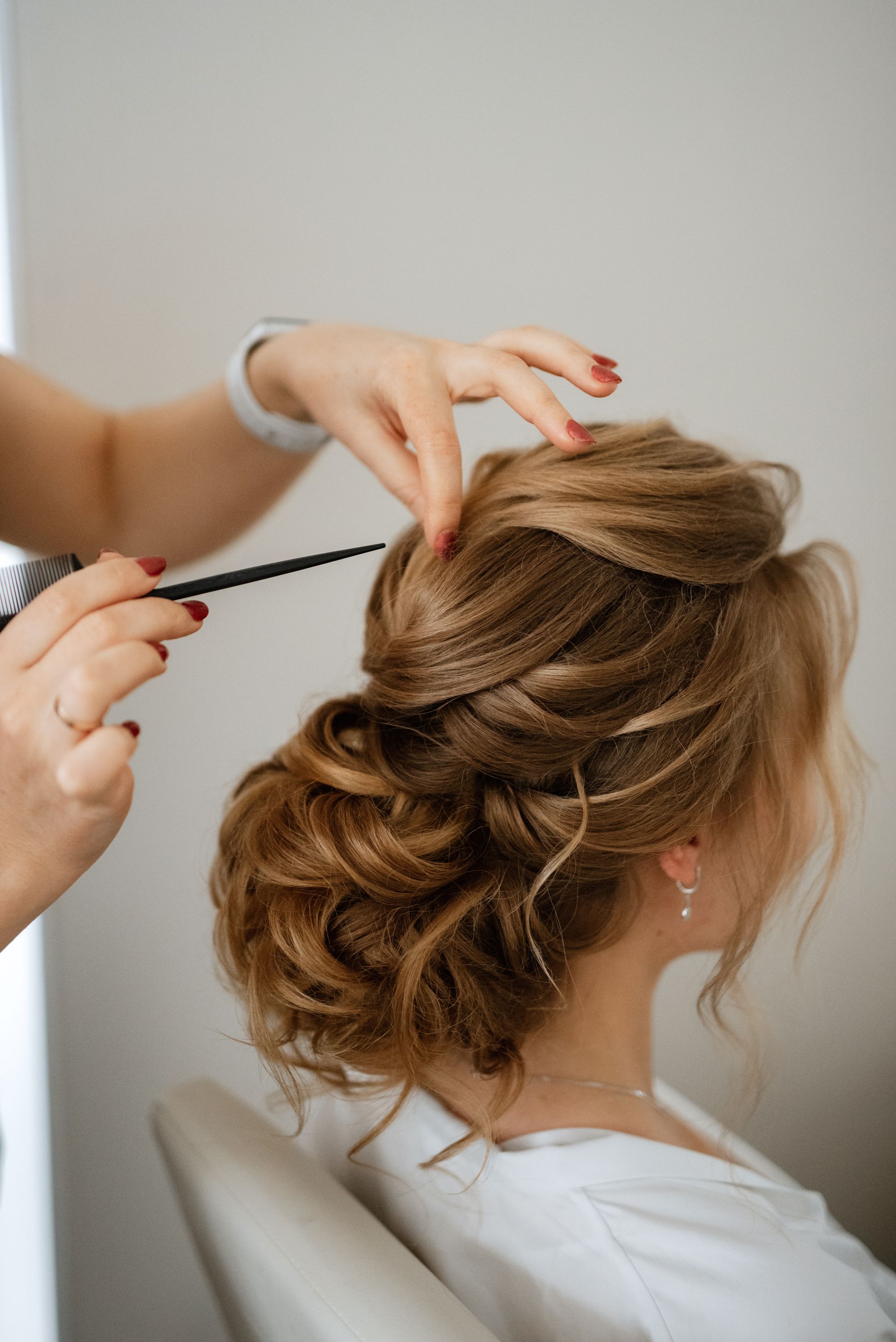 Une coiffeuse relève les cheveux d'une femme en un chignon élégant à l'aide d'un peigne.