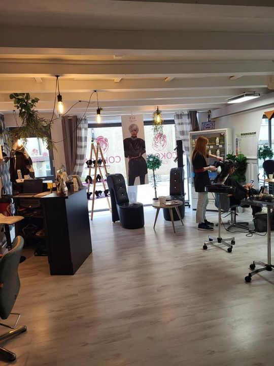 Intérieur de salon moderne avec fauteuils de coiffure, miroirs et personnes travaillant près des vitrines.