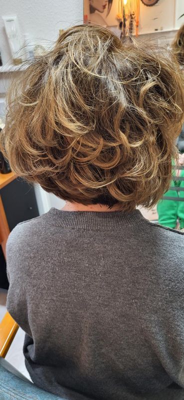 Vue de dos d'une coupe de cheveux courte et ondulée sur un fauteuil de salon, avec un pull visible.