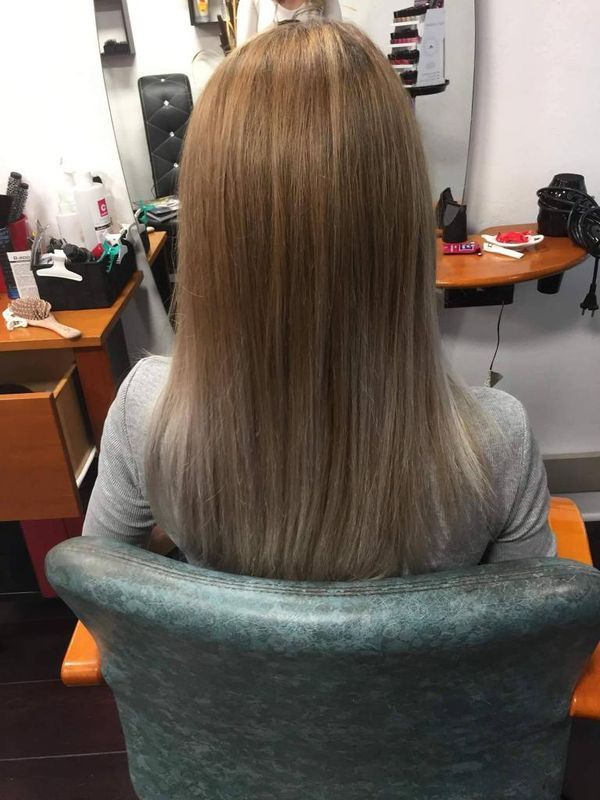 Une personne aux longs cheveux est assise dans un fauteuil de salon, vue de dos.