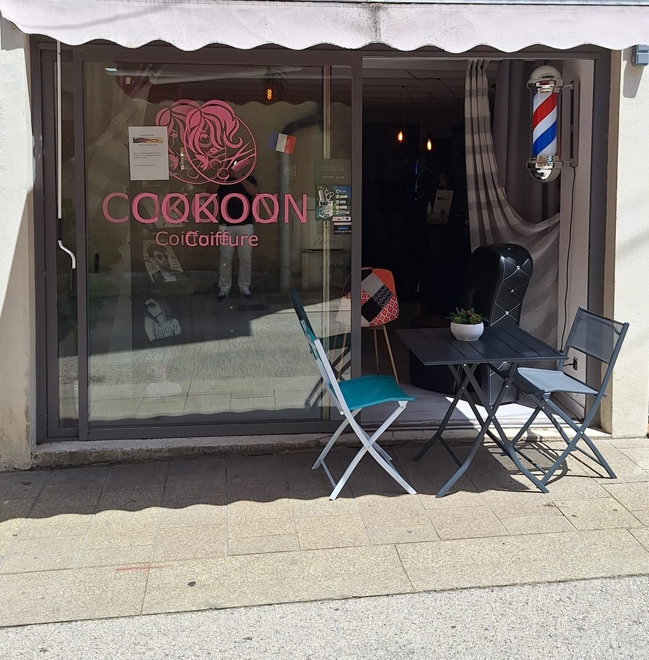 Façade du salon de coiffure Cokoon avec enseigne, vitrine, poteau de barbier et deux chaises à l'extérieur.