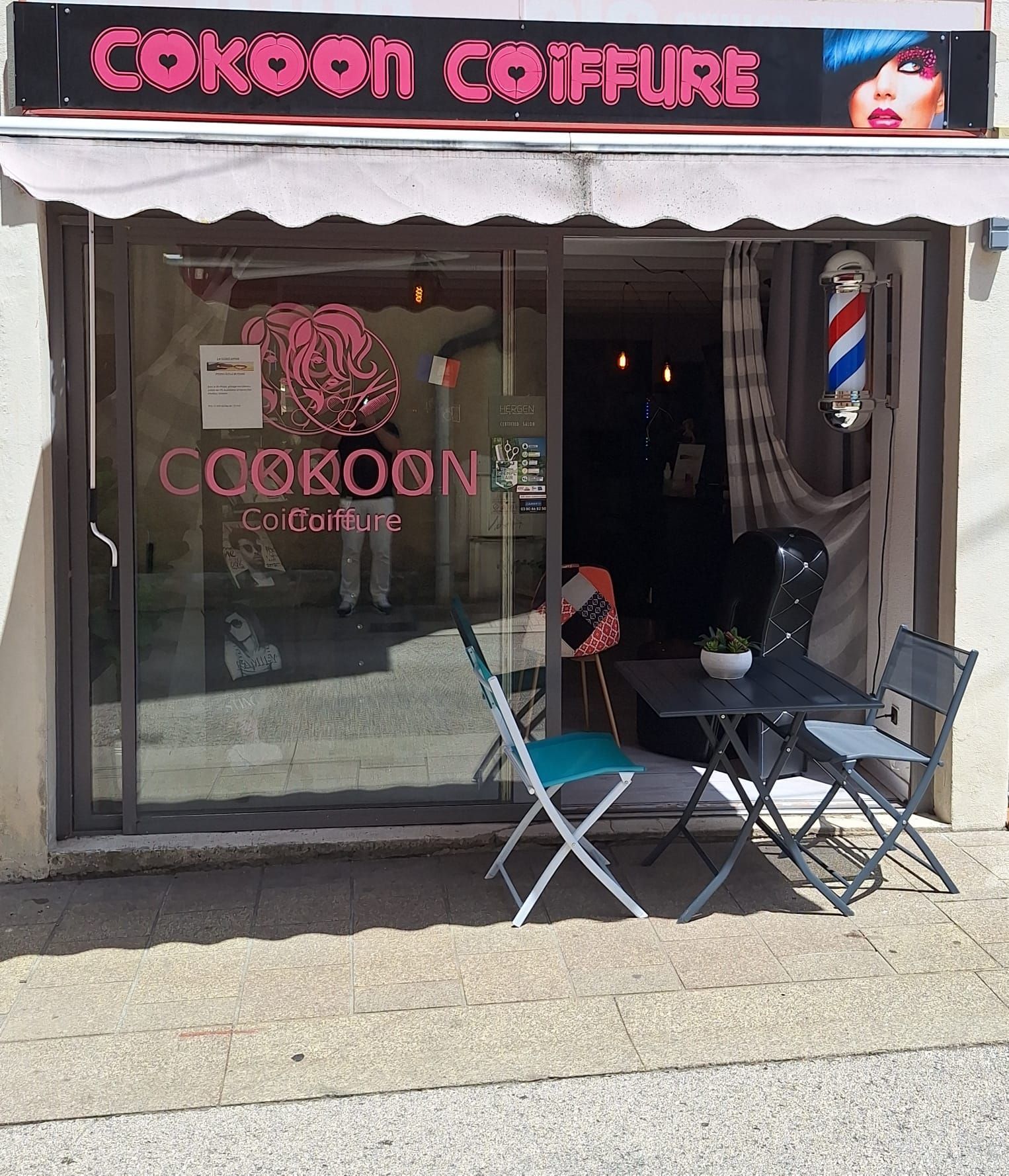 La façade du salon de coiffure Cokoon se distingue par son enseigne de barbier rayée, sa vitrine et sa petite terrasse.