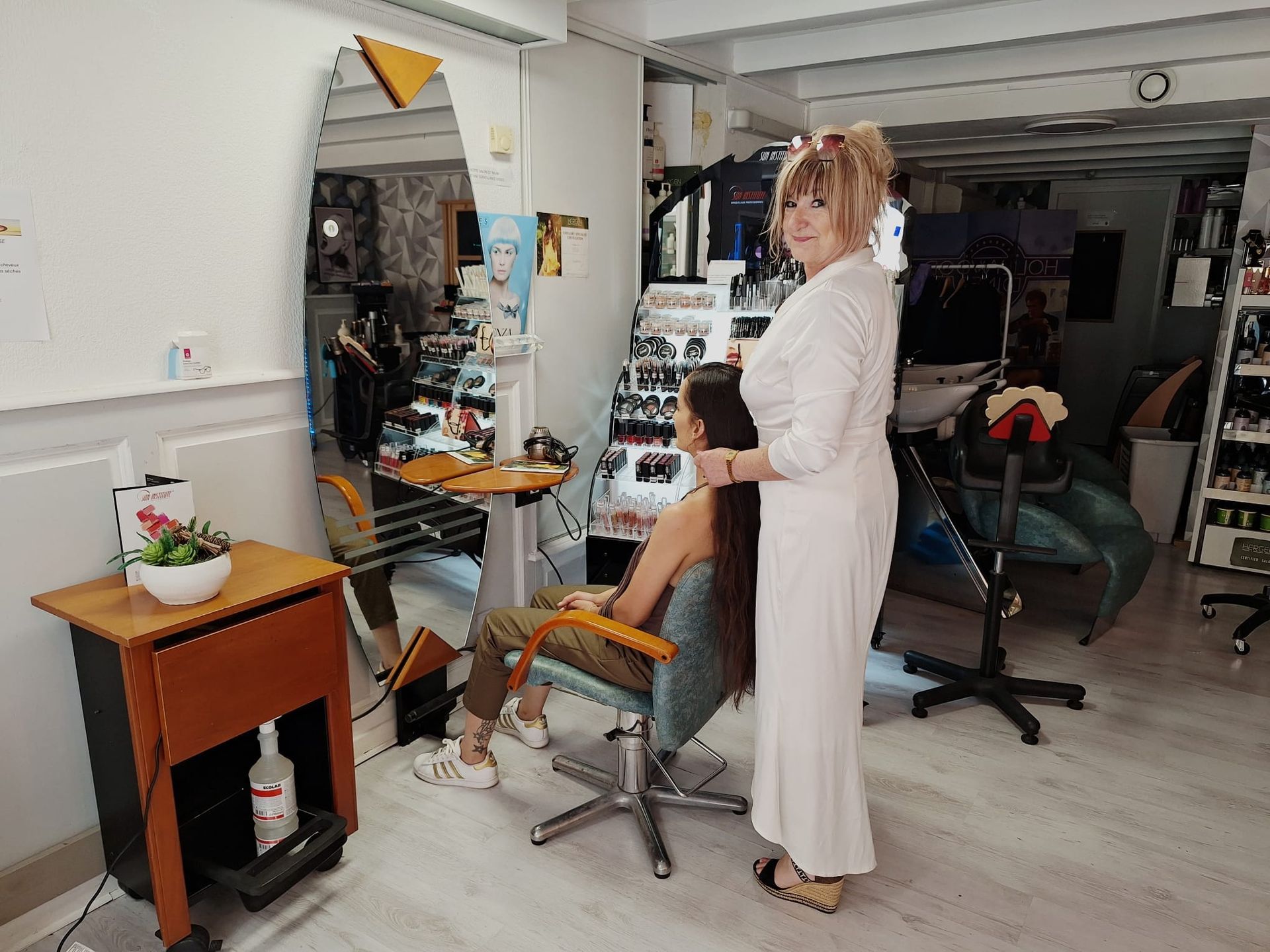 Une personne debout dans un salon de coiffure, tenant un outil de coiffure à côté d'un client assis.