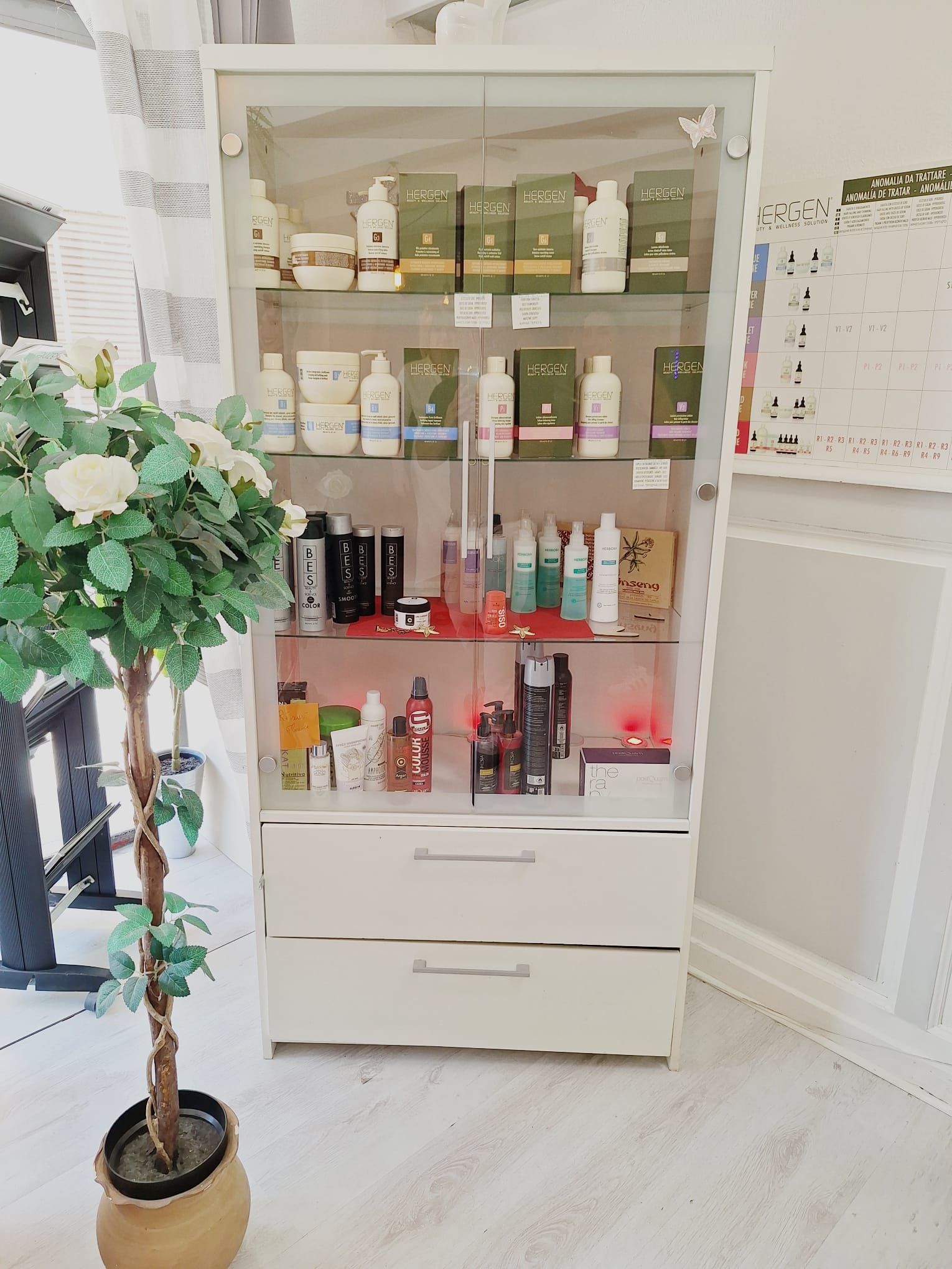 Vitrine contenant des produits et flacons de soins de la peau dans une pièce lumineuse, avec une plante en pot à côté.