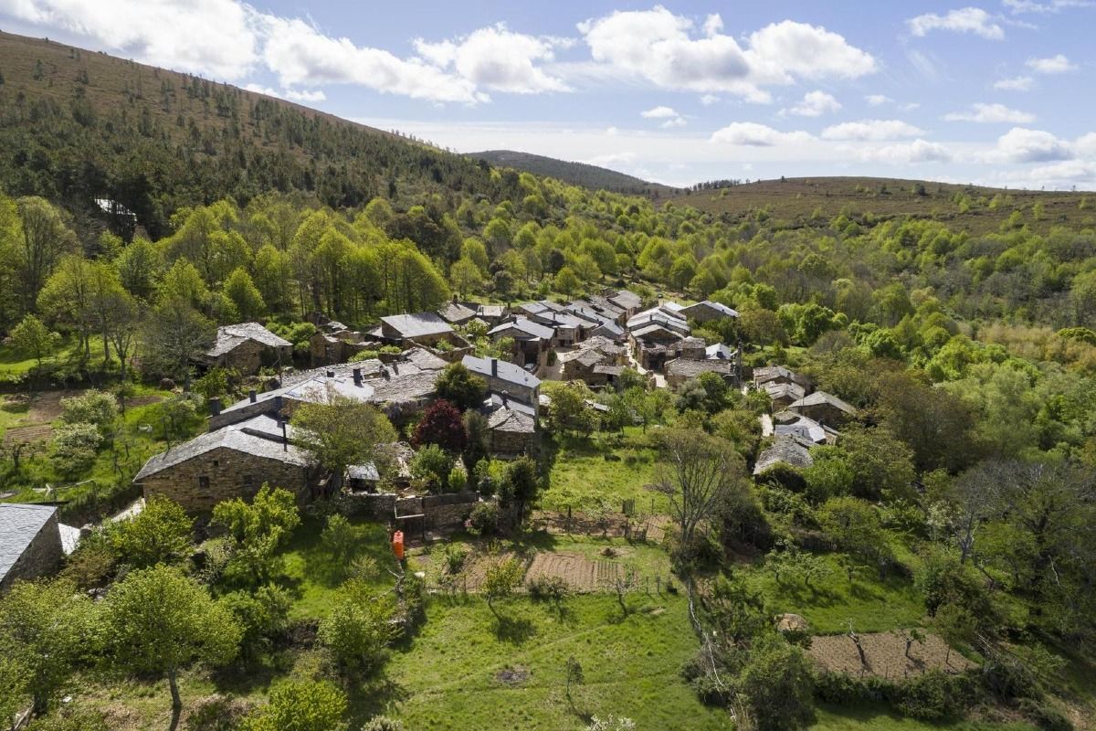 Vista aérea de una ciudad española con tejados de tejas rojas, un río y puentes. Día soleado con árboles y edificios.