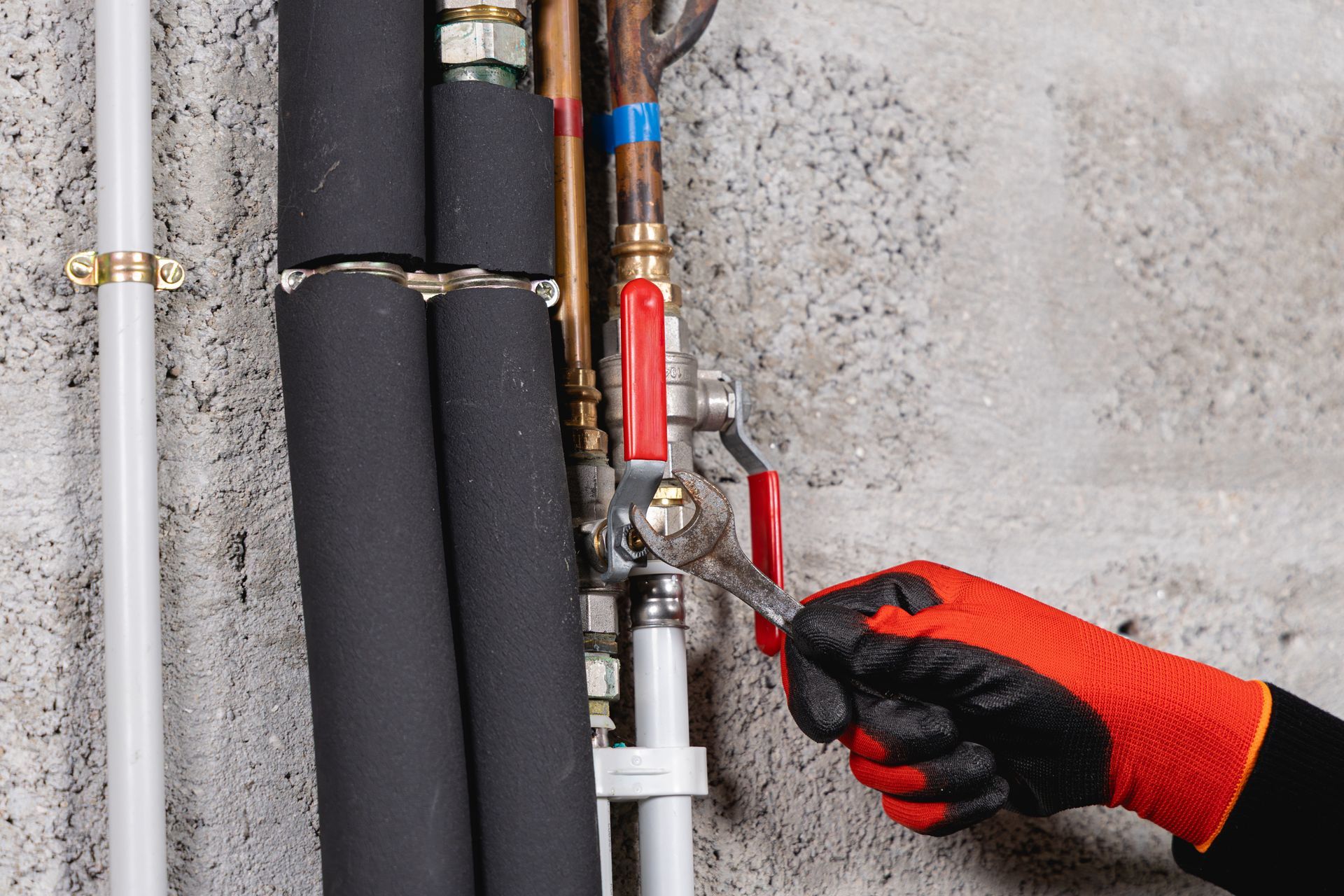 Une main gantée utilise une clé pour serrer une vanne sur un ensemble de plomberie contre un mur en béton.