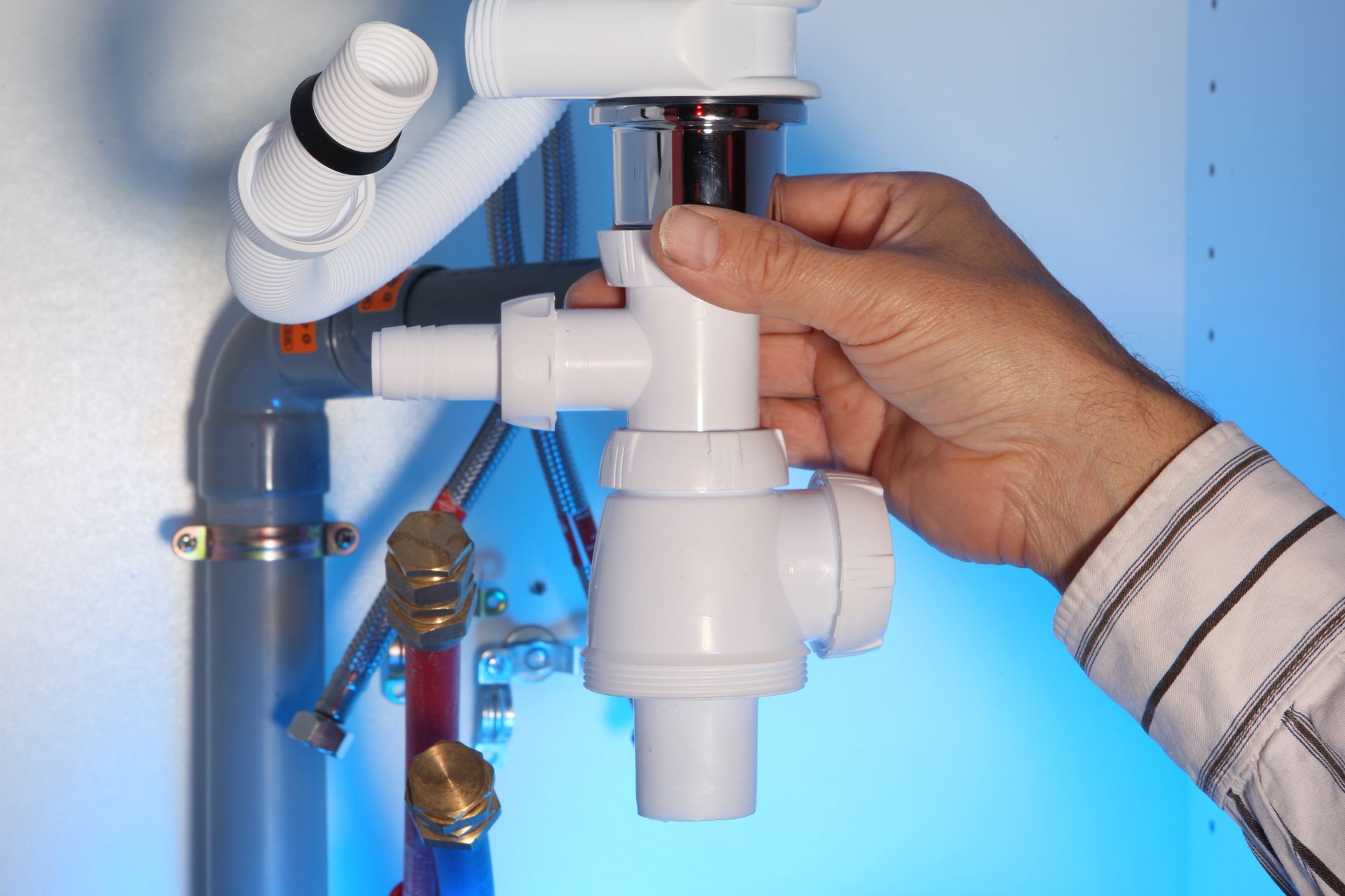 Une personne tient à la main un raccord de siphon en plastique blanc lors de son installation sur un système de tuyauterie d'évier.