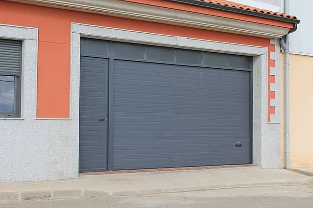 Una puerta de garaje gris está frente a una casa.