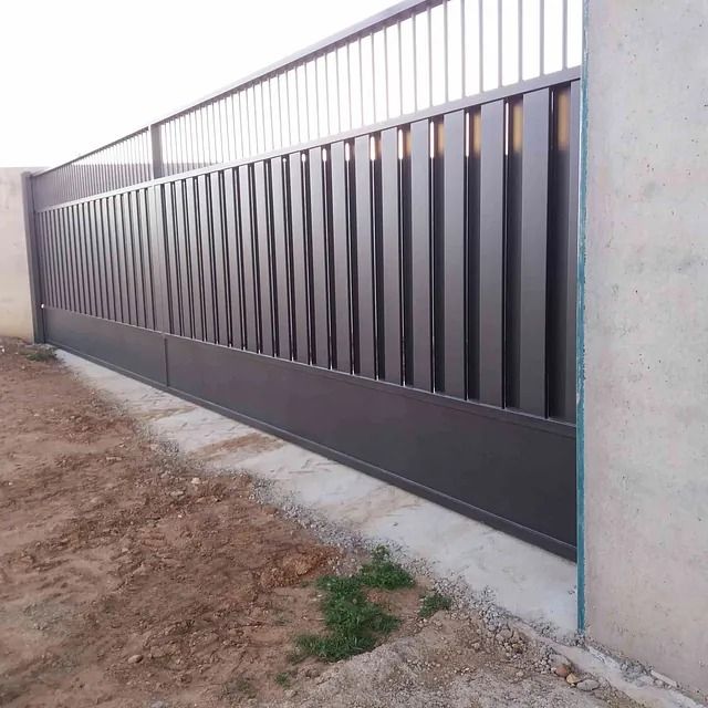 Una valla con puerta corrediza está rodeada de tierra y hierba.