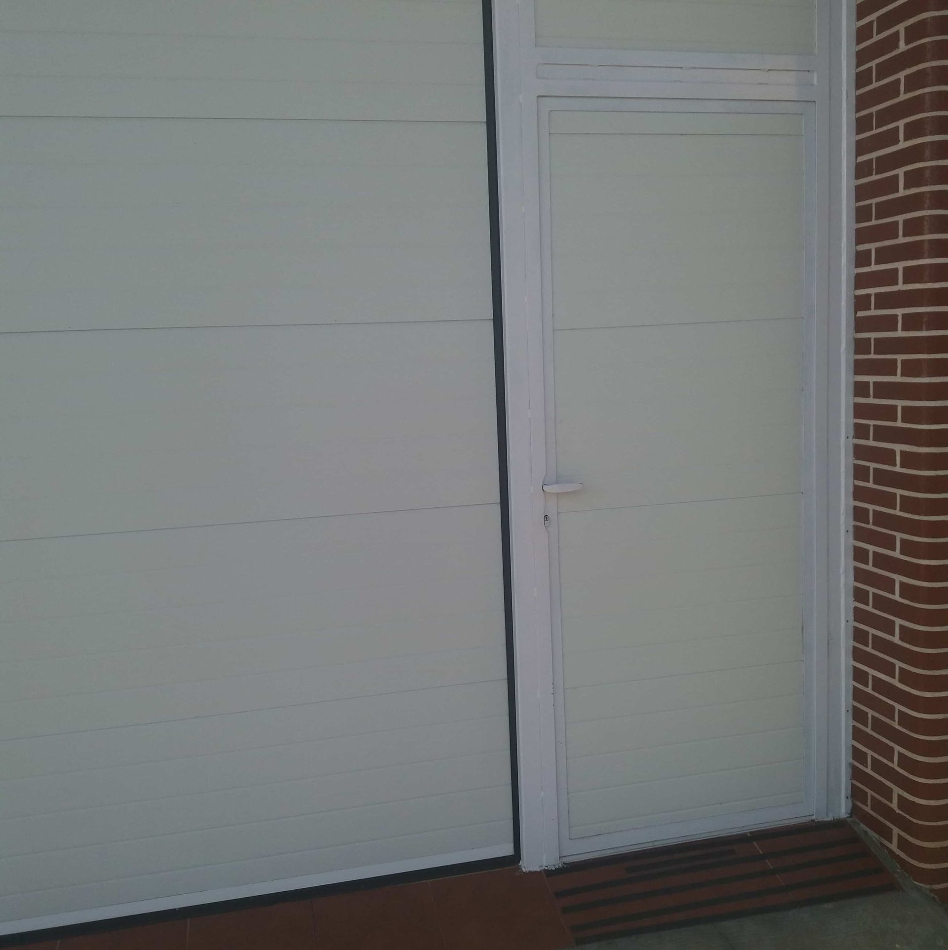 Una puerta de garaje blanca está al lado de una pared de ladrillos.