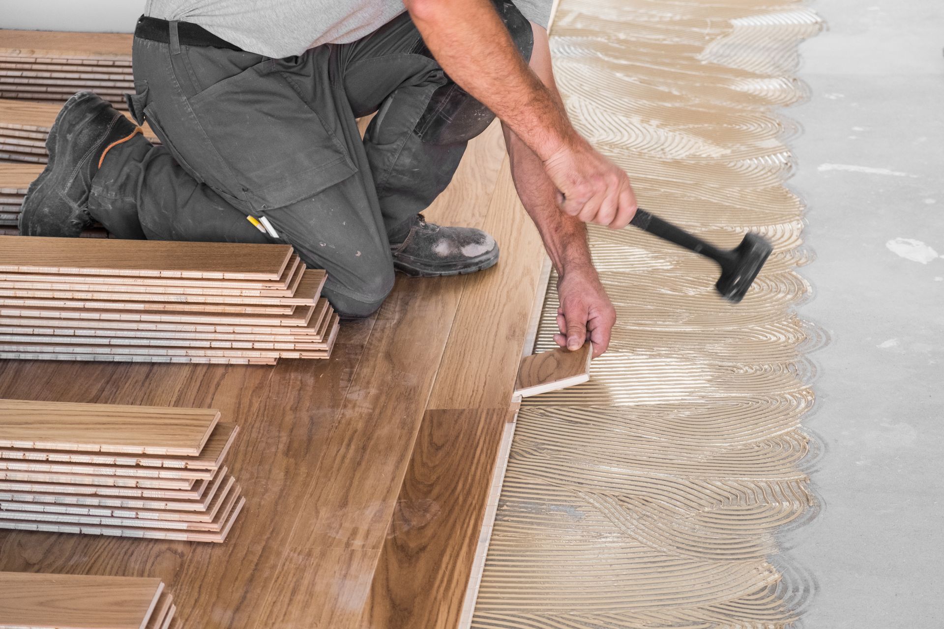 Un ouvrier agenouillé enfonce des lames de parquet dans une pièce en rénovation.
