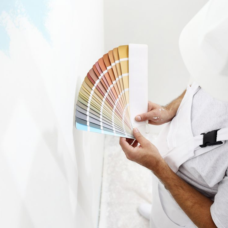 Une personne tenant un éventail d'échantillons de peinture contre un mur blanc