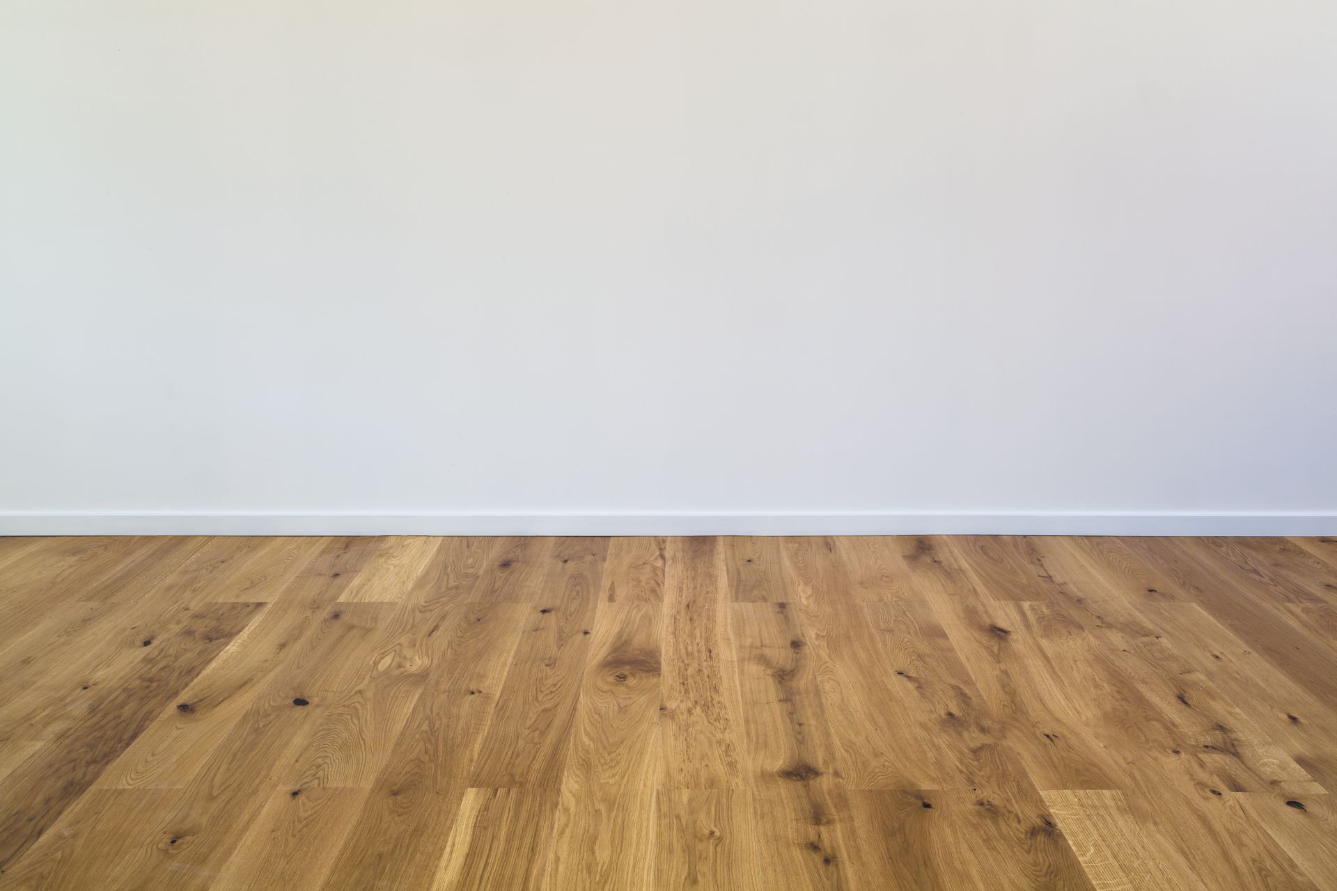 Pièce vide avec mur blanc, plinthe grise et parquet clair