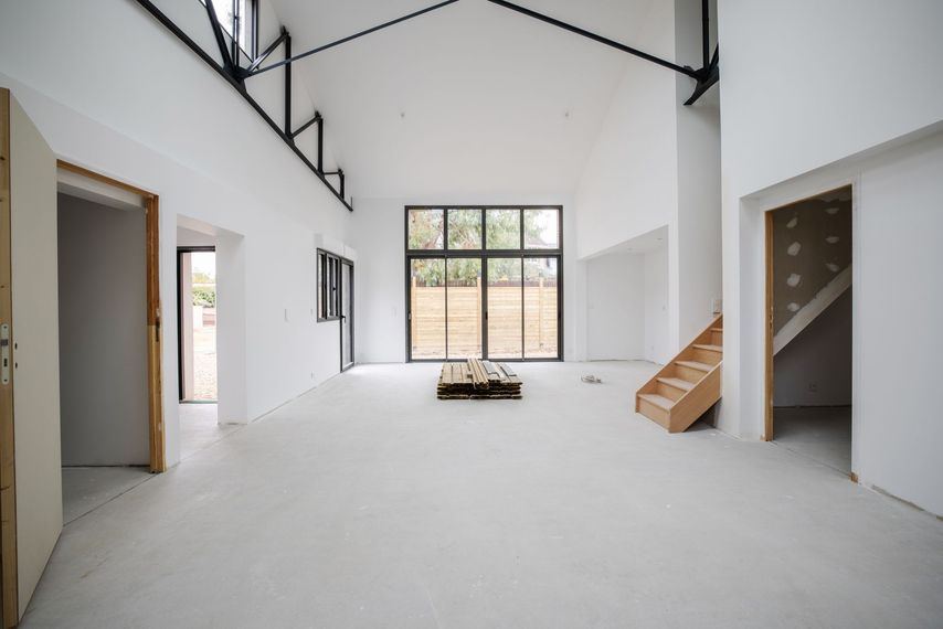 Intérieur d'un loft moderne vide avec hauts plafonds, murs blancs, grandes fenêtres et petit escalier.