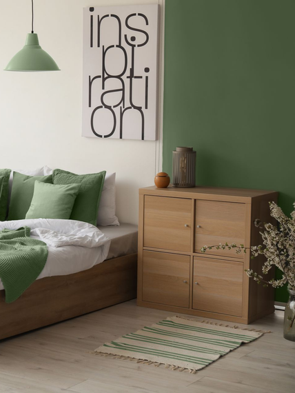 Chambre minimaliste verte avec lit en bois, petite armoire, décoration murale et tapis à rayures
