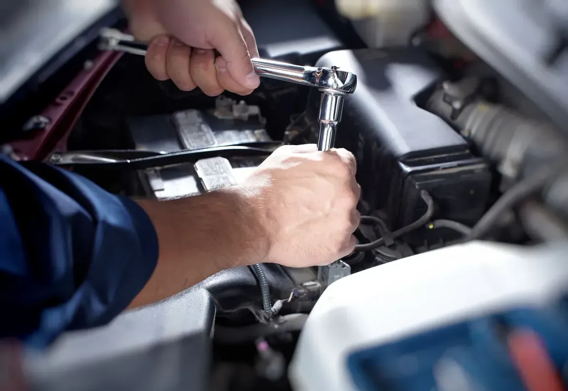 Un hombre está trabajando en el motor de un automóvil con una llave inglesa.