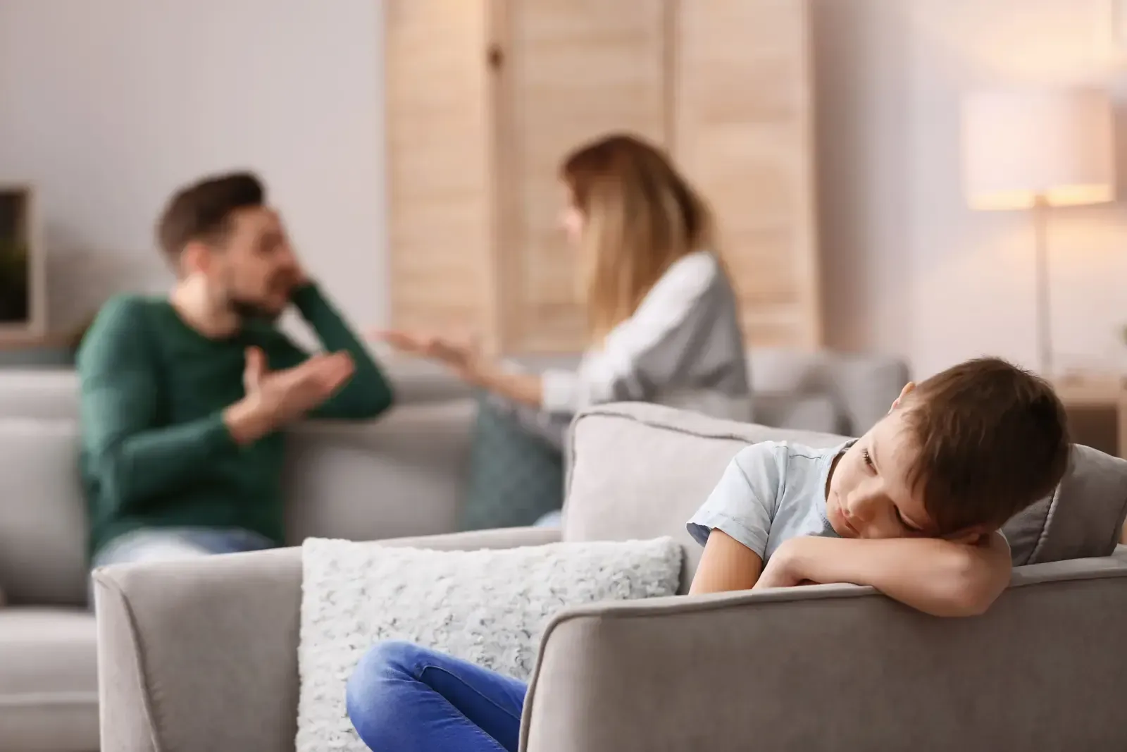 Ein Junge sitzt auf einem Sofa, während im Hintergrund seine Eltern streiten.