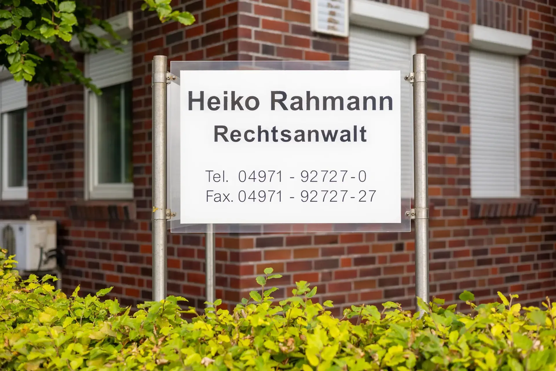 Auf einem Schild vor einem Backsteingebäude steht Heiko Rahmann Rechtsanwalt