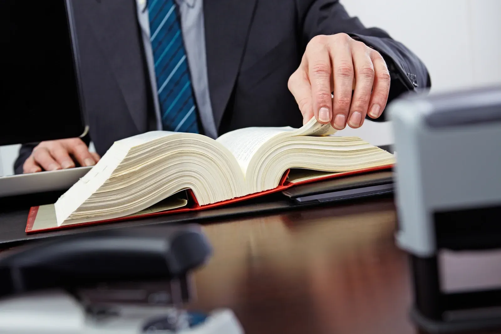 Ein Mann in Anzug und Krawatte sitzt an einem Schreibtisch und liest ein Buch.