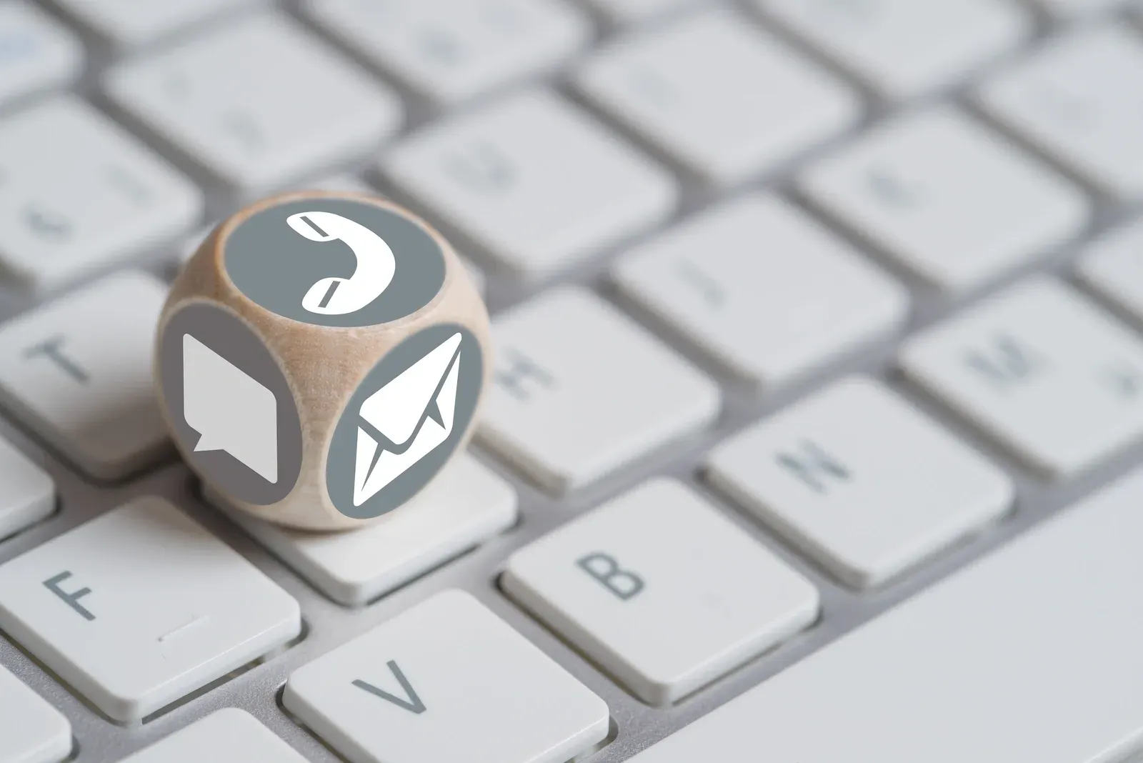 Auf einer Tastatur liegt ein Holzwürfel mit einem Telefonumschlag und einer Sprechblase darauf.