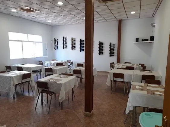 Comedor vacío con manteles blancos, mesas de madera y una columna de soporte central.
